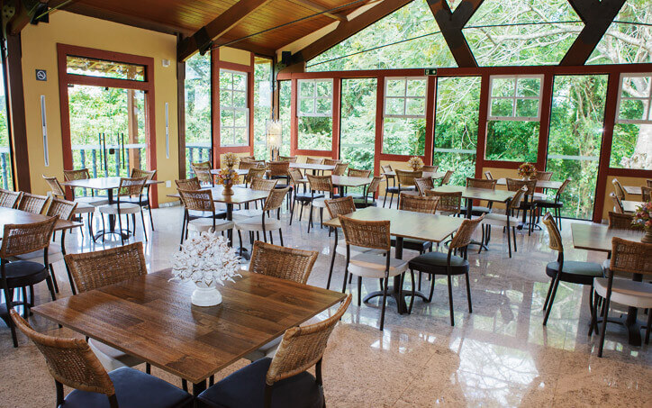 Visão do restaurante-escola de Tiradentes, com mesas amplas e janelas de vidro para espaço arborizado. 
